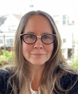 White woman with light colored long hair and dark rimmed glasses